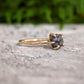 Raw black diamond engagement ring on a stone surface with a 14k gold band, showcasing a unique uncut design.