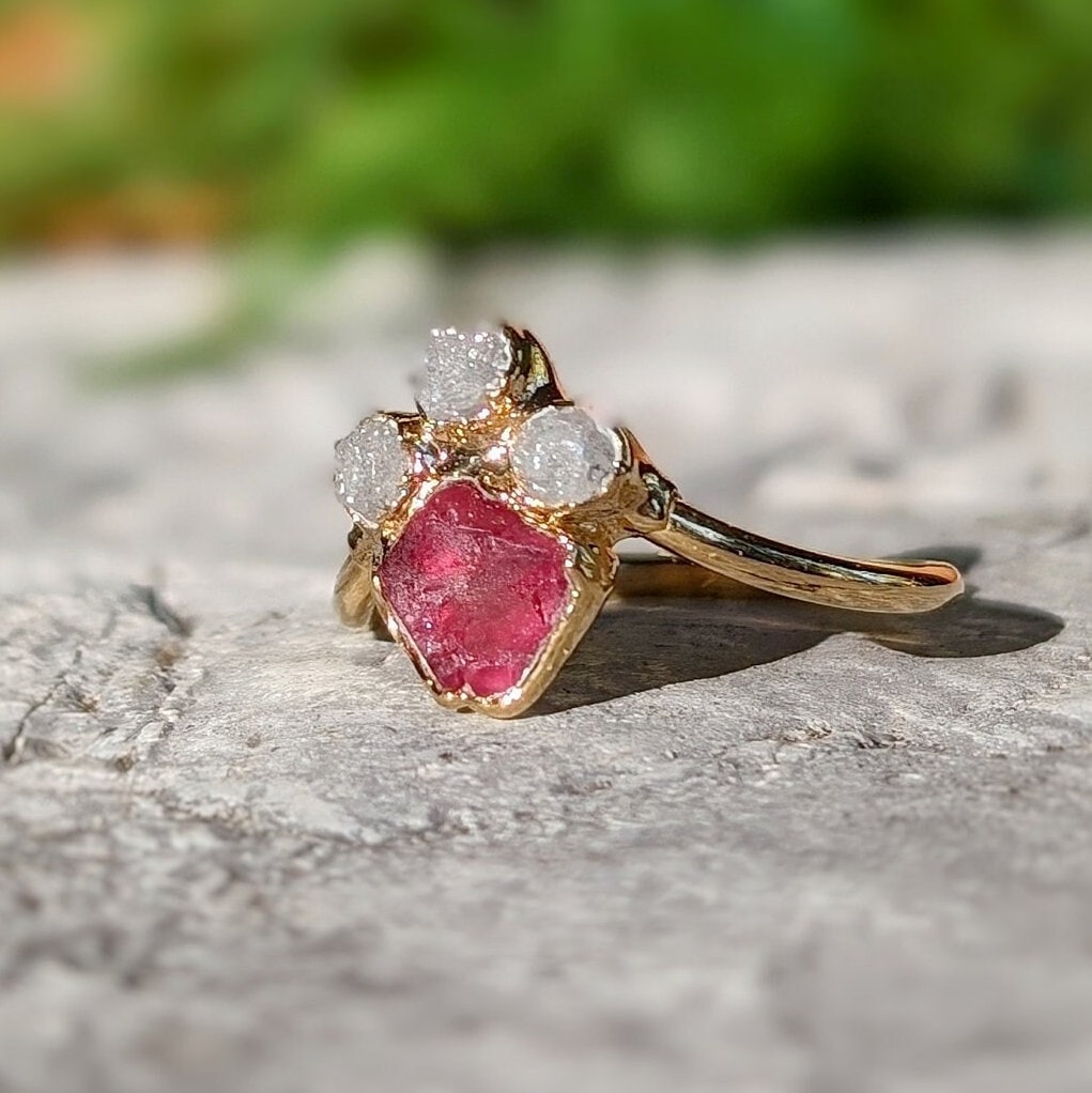 Raw diamond and pink spinel chevron engagement ring displayed on a textured surface, showcasing its unique design.
