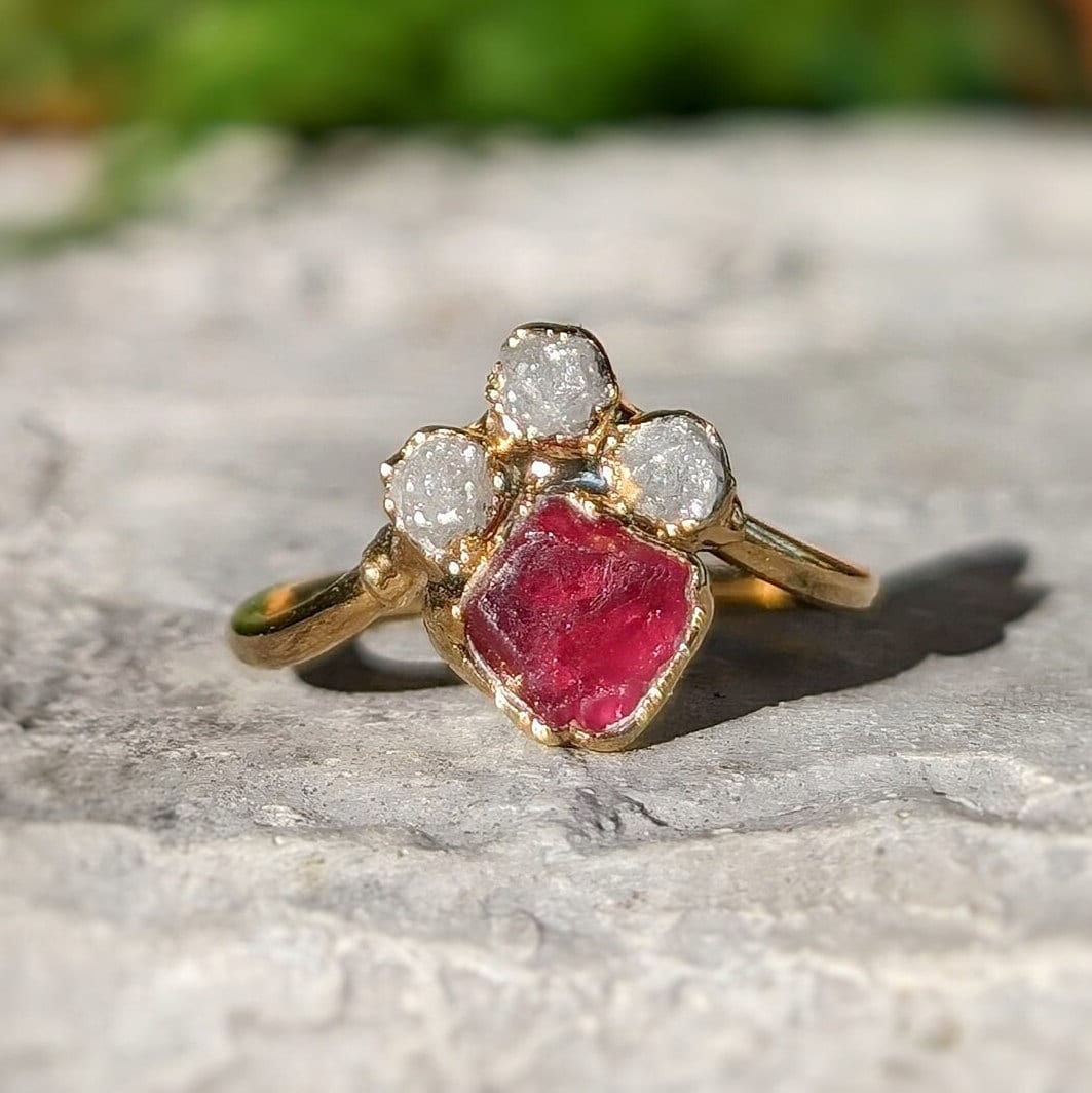 Raw diamond and pink spinel chevron engagement ring on a rocky surface, showcasing unique handcrafted beauty.