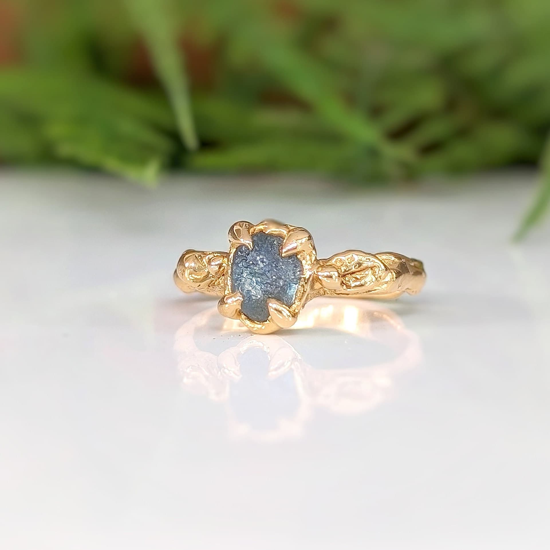 Raw Montana Sapphire engagement ring in solid 14k gold with an intricately textured band, showcasing unique elegance.