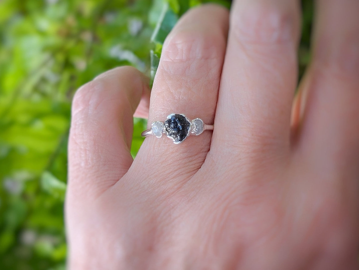 Raw black diamond engagement ring on hand, featuring a large uncut diamond and small accent stones on a silver band.