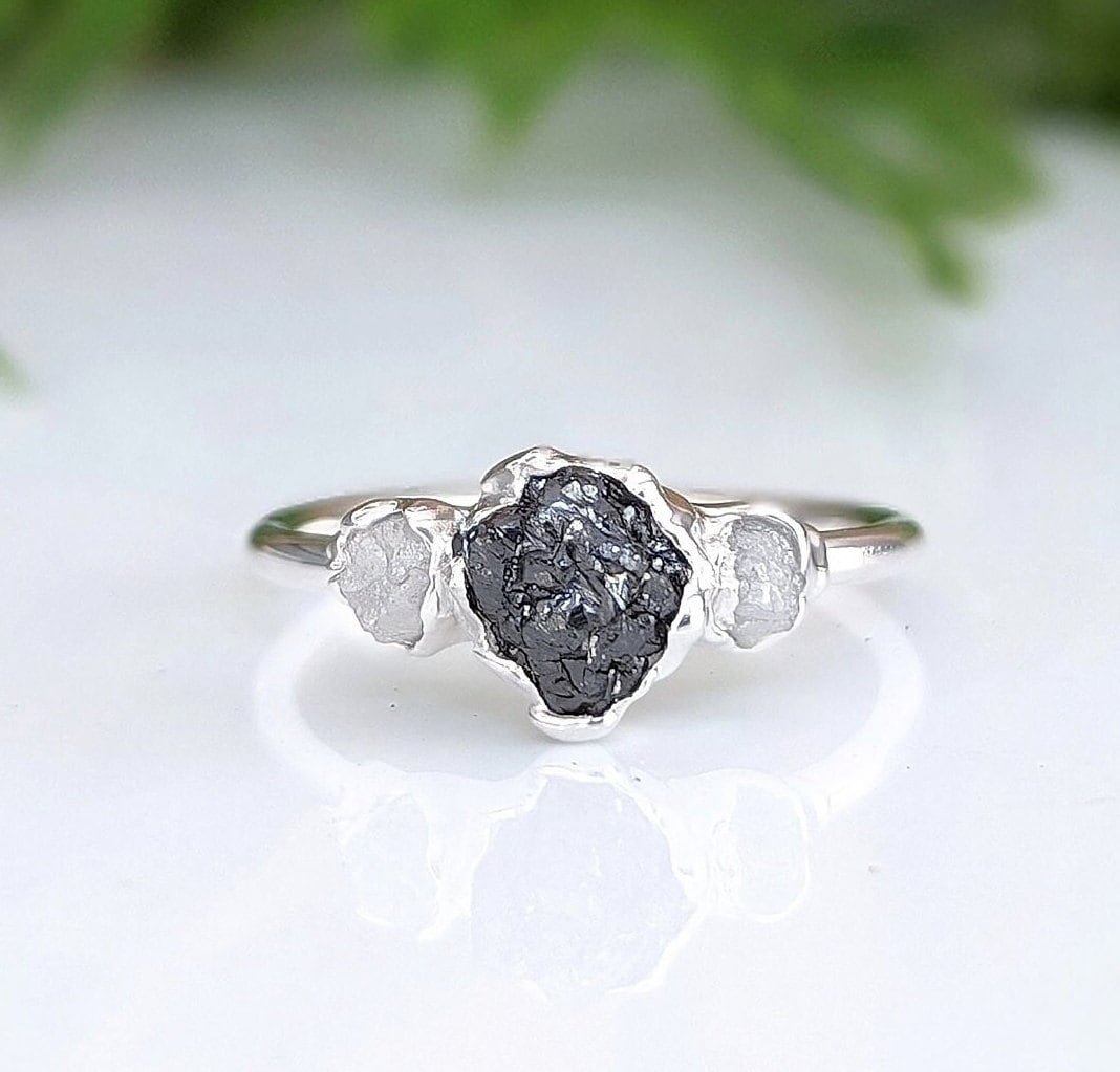 Raw black diamond engagement ring on a sterling silver band with two smaller diamonds, showcasing unique handcrafted design.