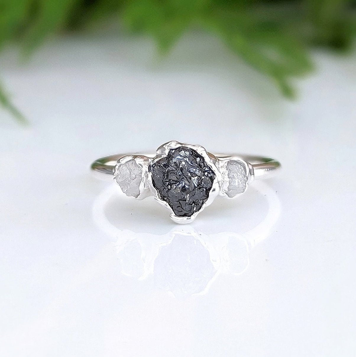 Raw black diamond engagement ring on sterling silver band, featuring uncut diamond and two smaller rough diamonds.