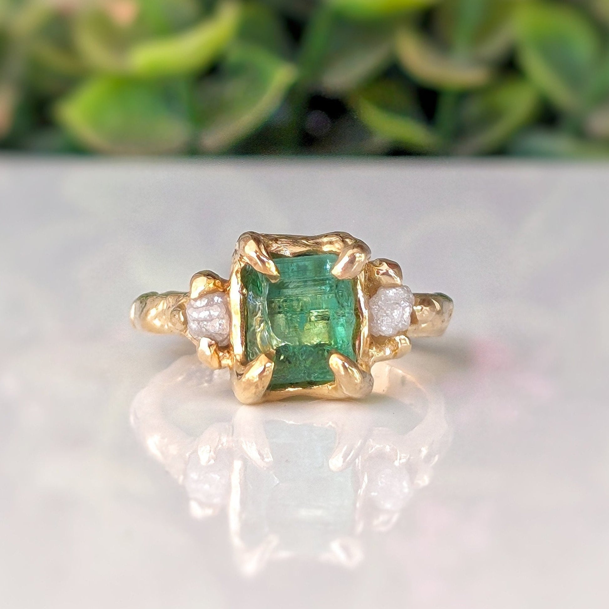 Raw emerald and diamond engagement ring in solid 14k gold, featuring a mint green emerald and two small diamonds.