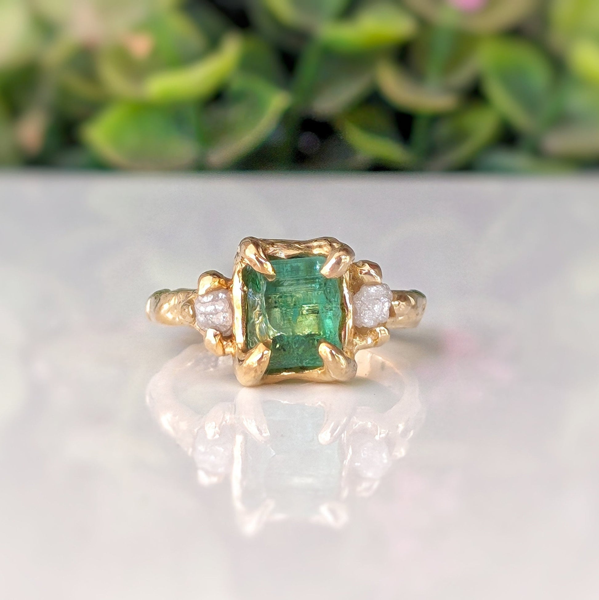 Raw emerald and diamond engagement ring in gold, showcasing a mint green emerald and two small conflict-free diamonds.