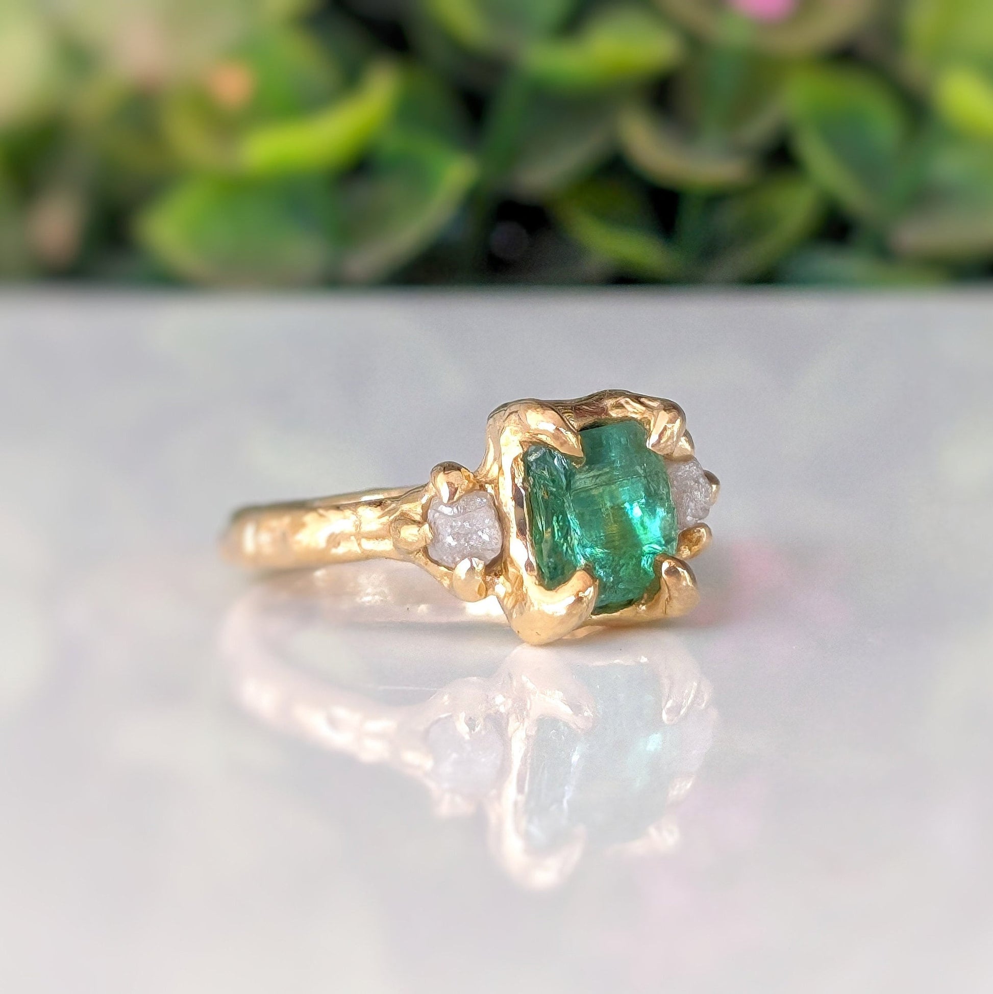 Raw emerald and diamond engagement ring in solid 14k gold, featuring a mint green emerald and two raw diamonds.
