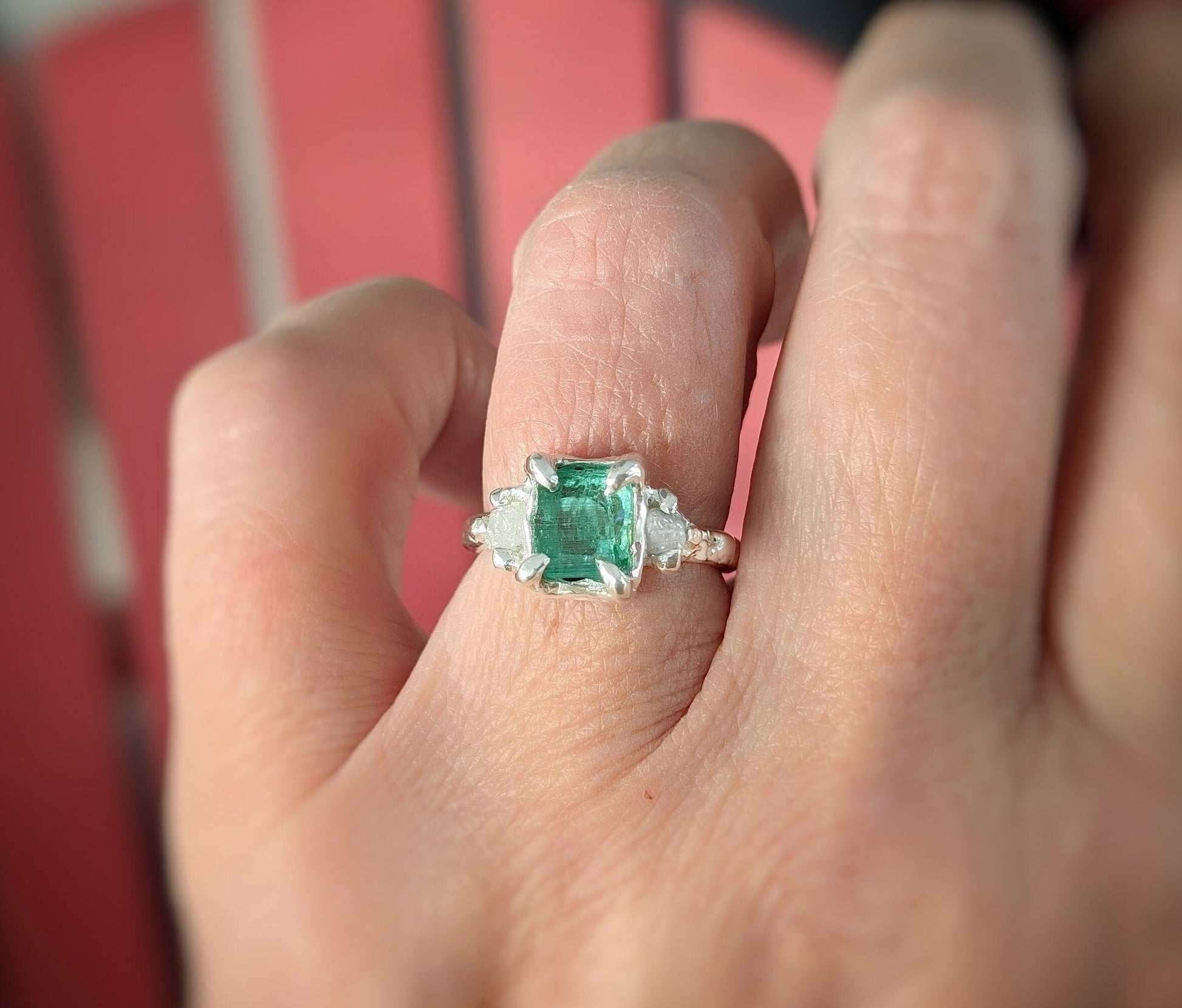 Hand wearing a raw emerald and diamond engagement ring set in solid 14k gold, showcasing its unique natural beauty.