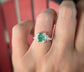 Hand wearing a raw emerald and diamond engagement ring set in solid 14k gold, showcasing its unique natural beauty.