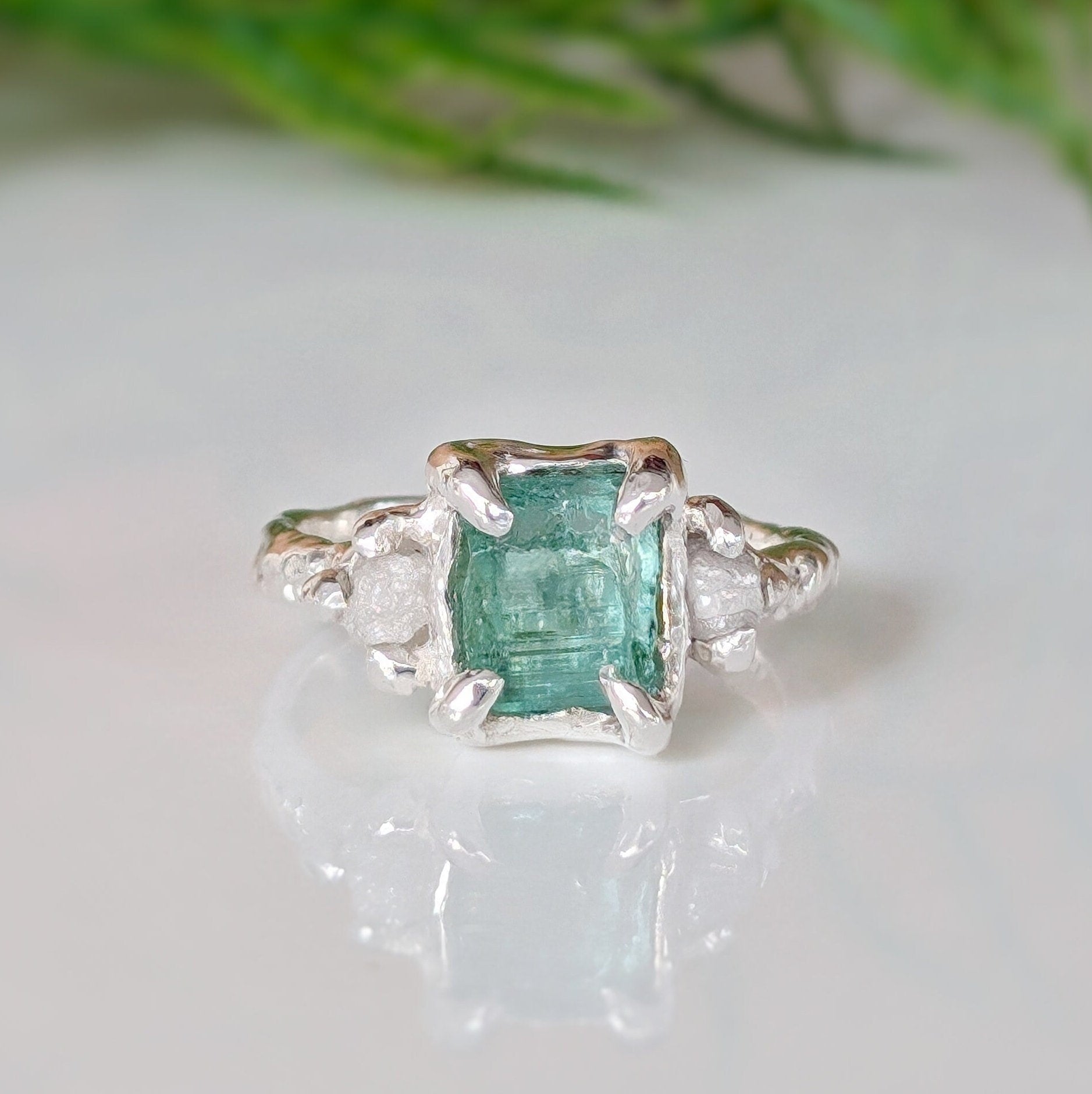 Raw emerald and diamond engagement ring in solid 14k gold, featuring a mint green emerald and two small raw diamonds.