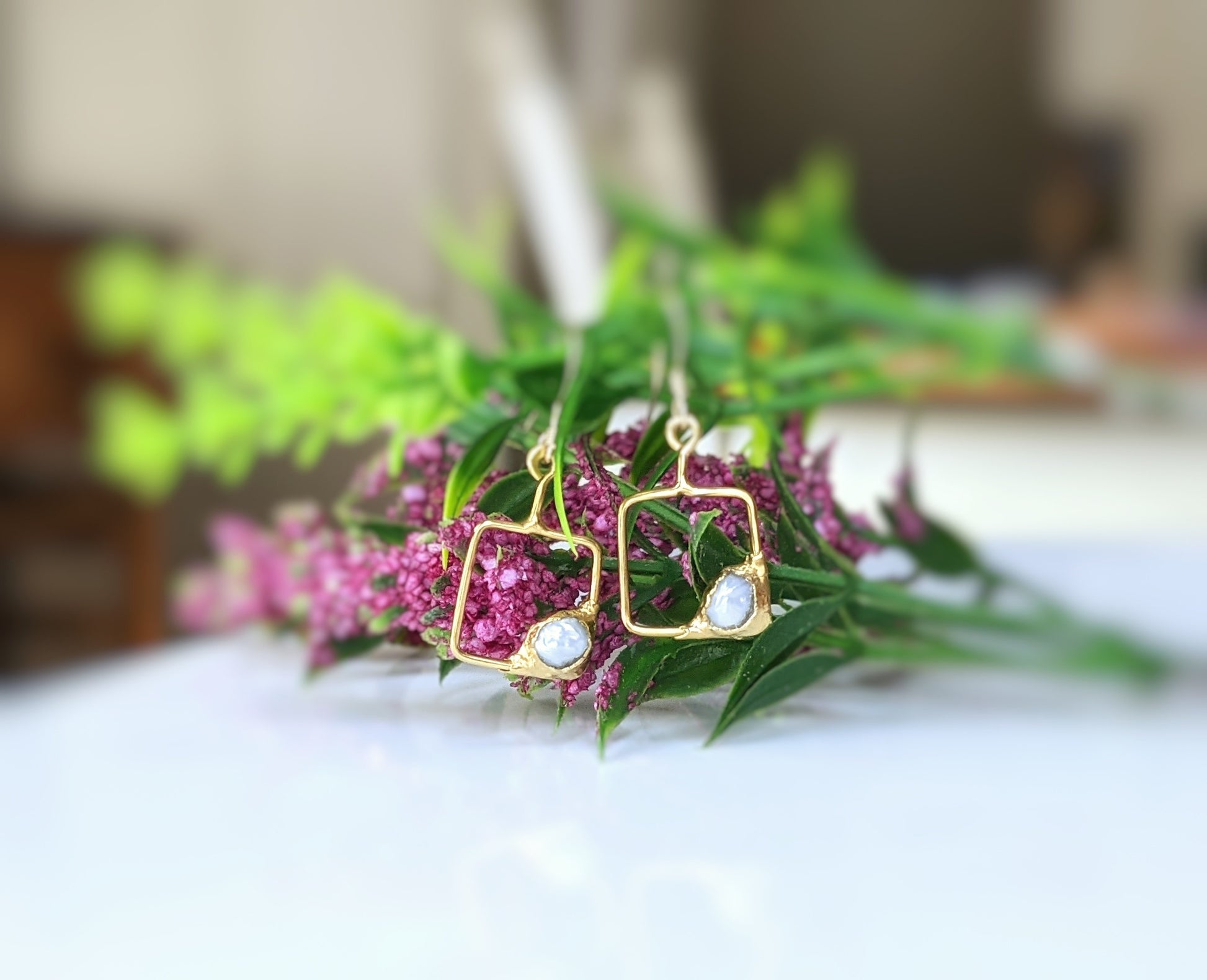 Keshi pearl square dangle earrings in gold setting, showcasing delicate design against a floral backdrop.