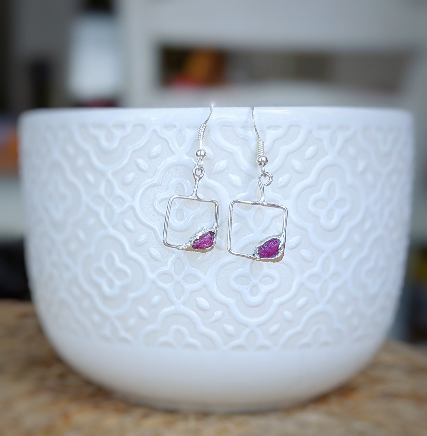 Delicate square earrings featuring pink gemstones set in sterling silver, displayed in a textured white bowl.