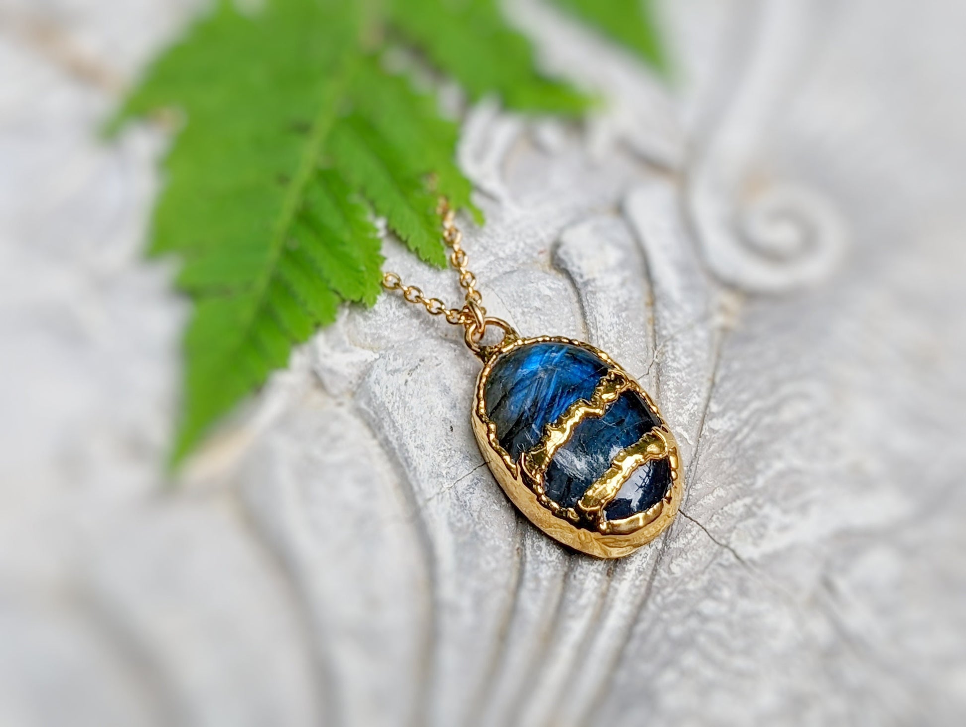 Labradorite Kintsugi necklace with gold plating on a textured background and green leaf.