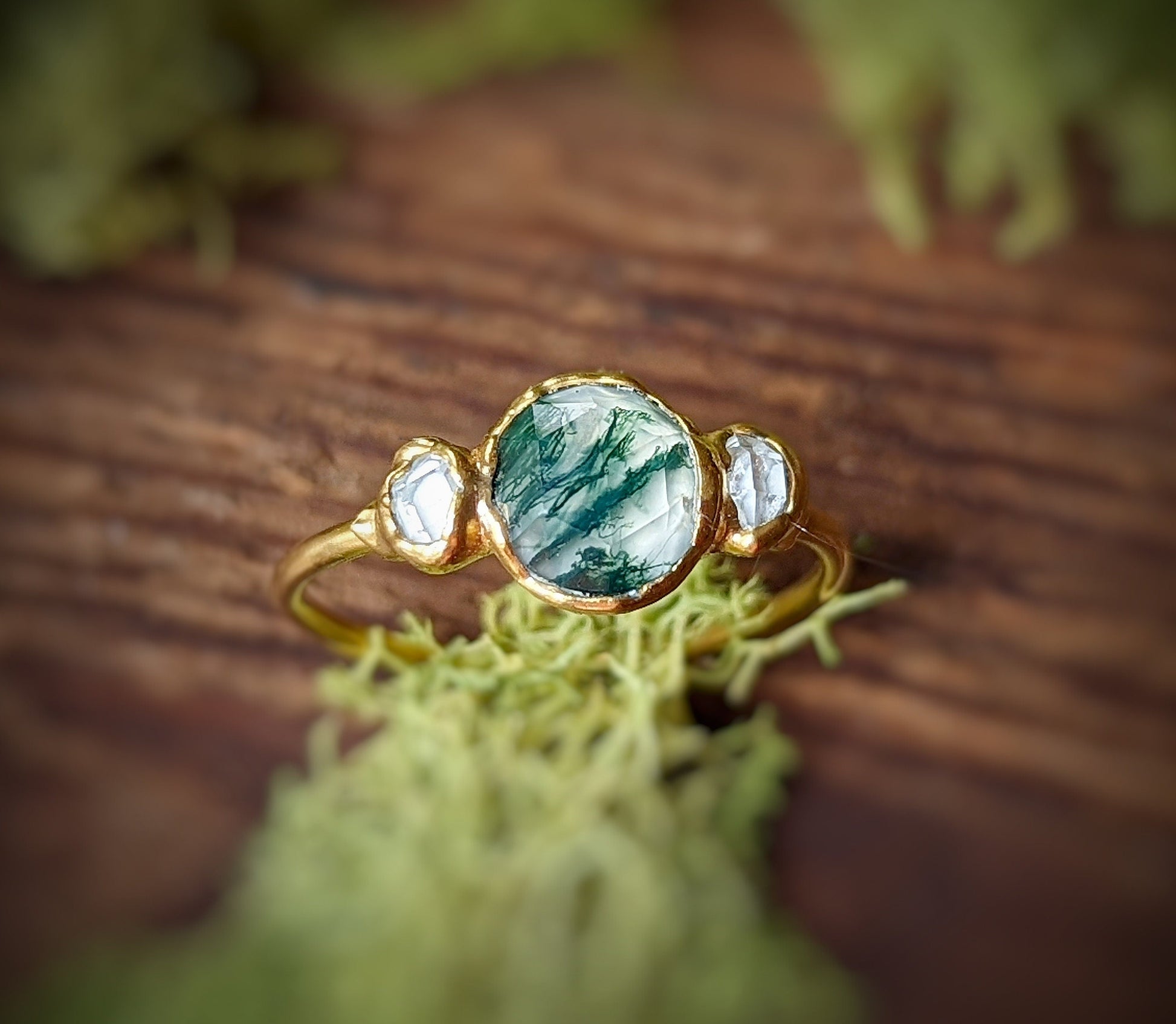 Handcrafted Moss Agate ring with Herkimer diamonds on an 18k gold band, set against rustic moss background.