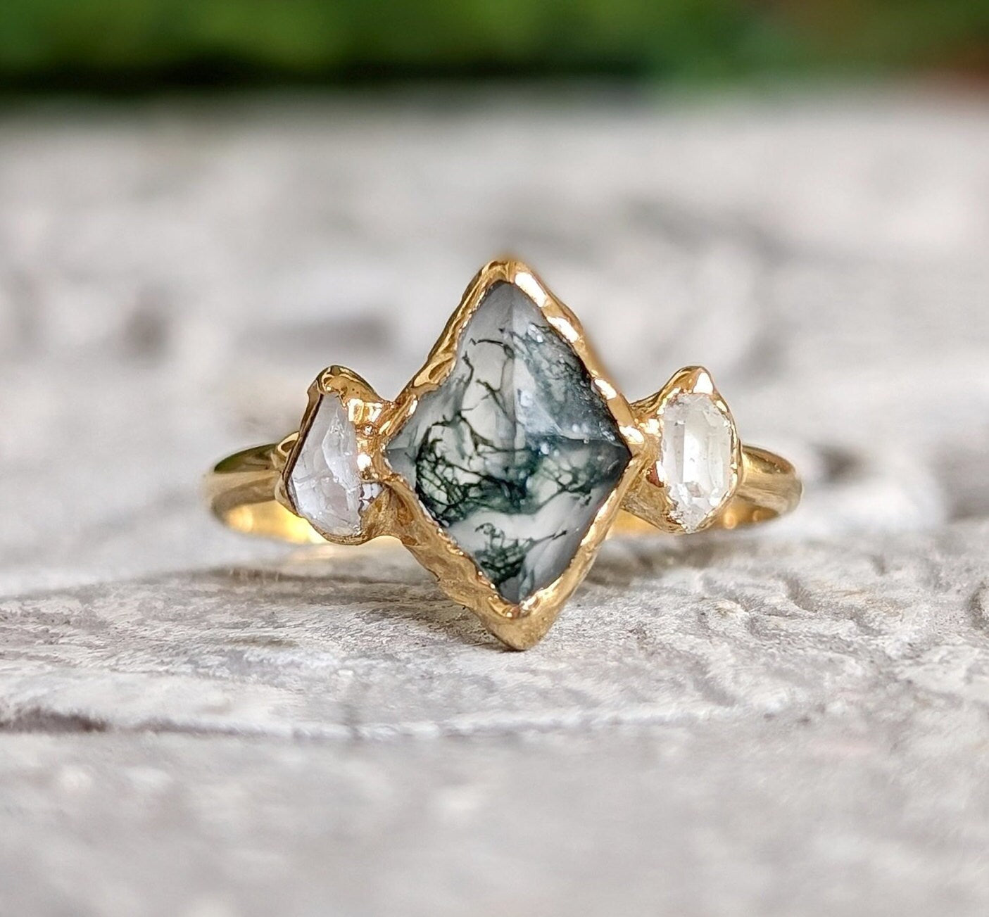 Moss Agate and Herkimer diamond engagement ring on a textured surface. Unique lozenge shape, 14k gold band.