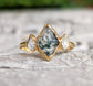 Moss Agate and Herkimer diamond engagement ring on a textured surface. Unique lozenge shape, 14k gold band.