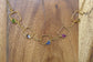 Unique gold square pendant necklace featuring colorful raw gemstones on a wooden background.