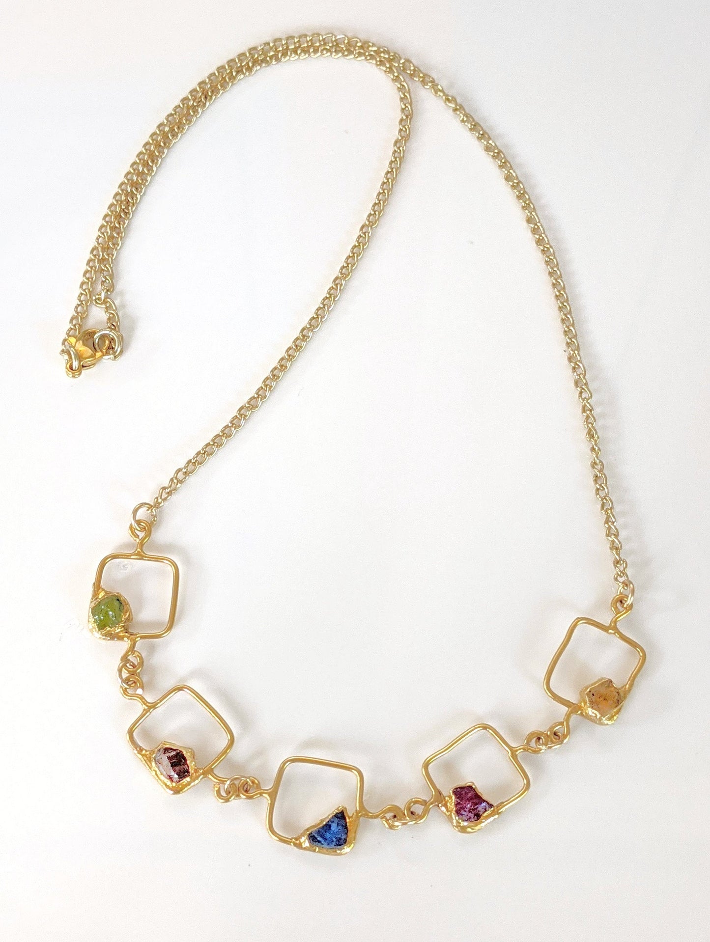 Personalized family birthstone necklace featuring raw gemstones in square settings with a gold chain.