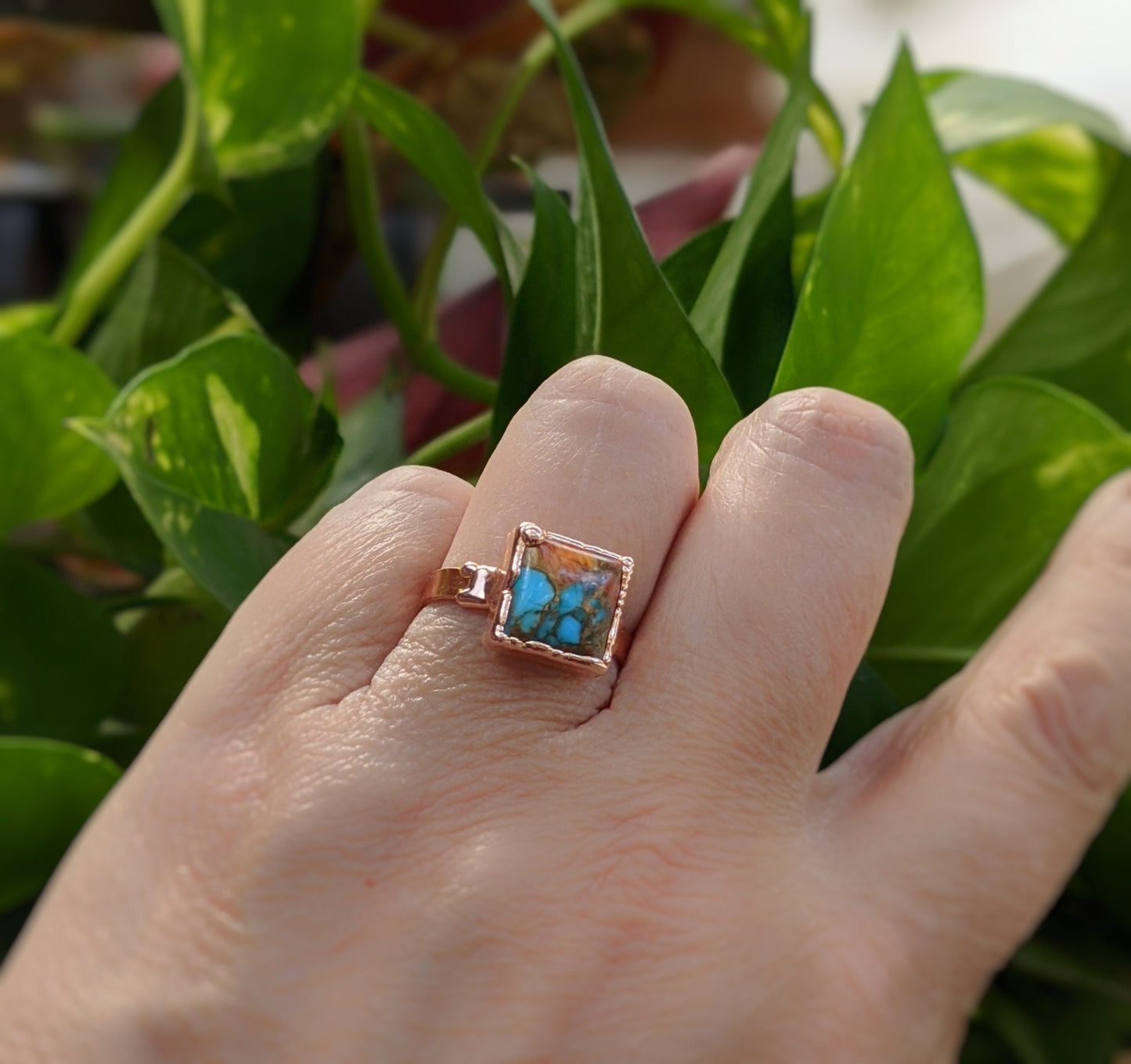 Handcrafted pink opal copper turquoise ring on a hand, showcasing natural gemstones against vibrant green leaves.