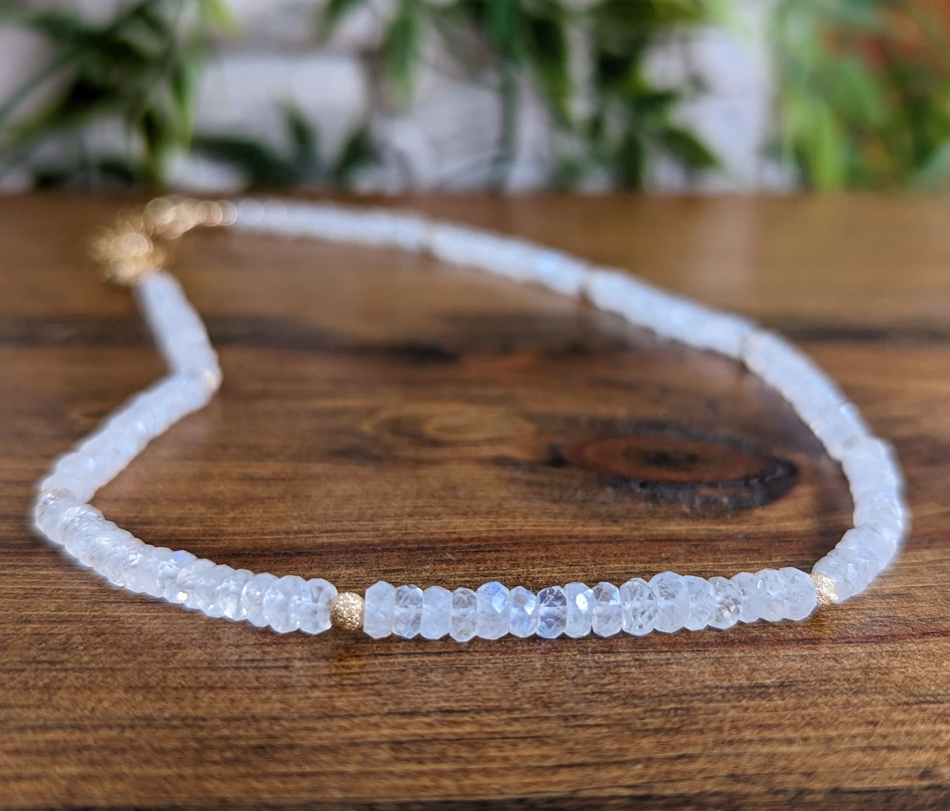 Dainty rainbow Moonstone faceted beaded necklace on wooden surface, showcasing ethereal beauty and elegance.