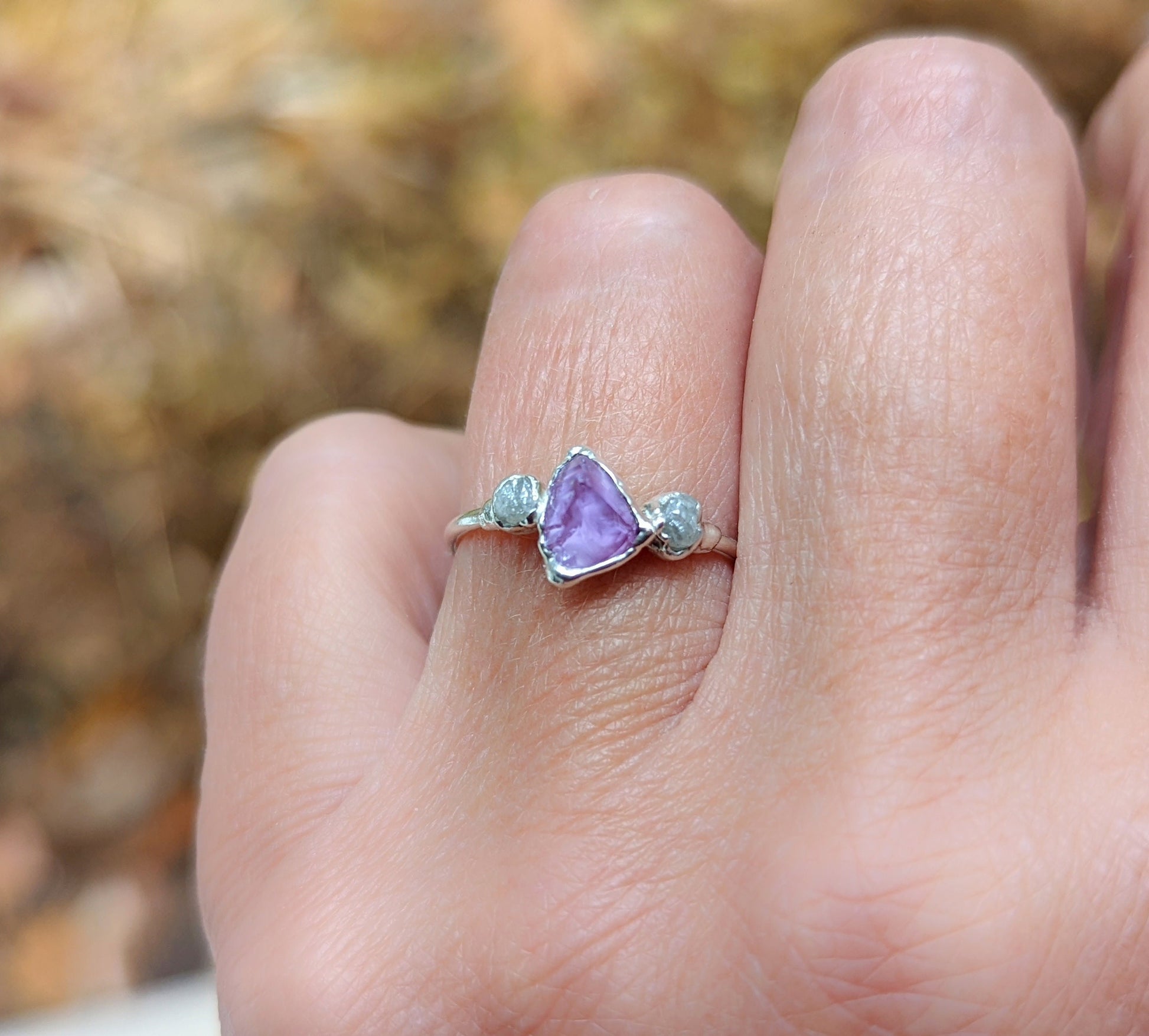 Hand wearing a raw Alexandrite and diamond silver ring, showcasing unique gemstones in natural light.