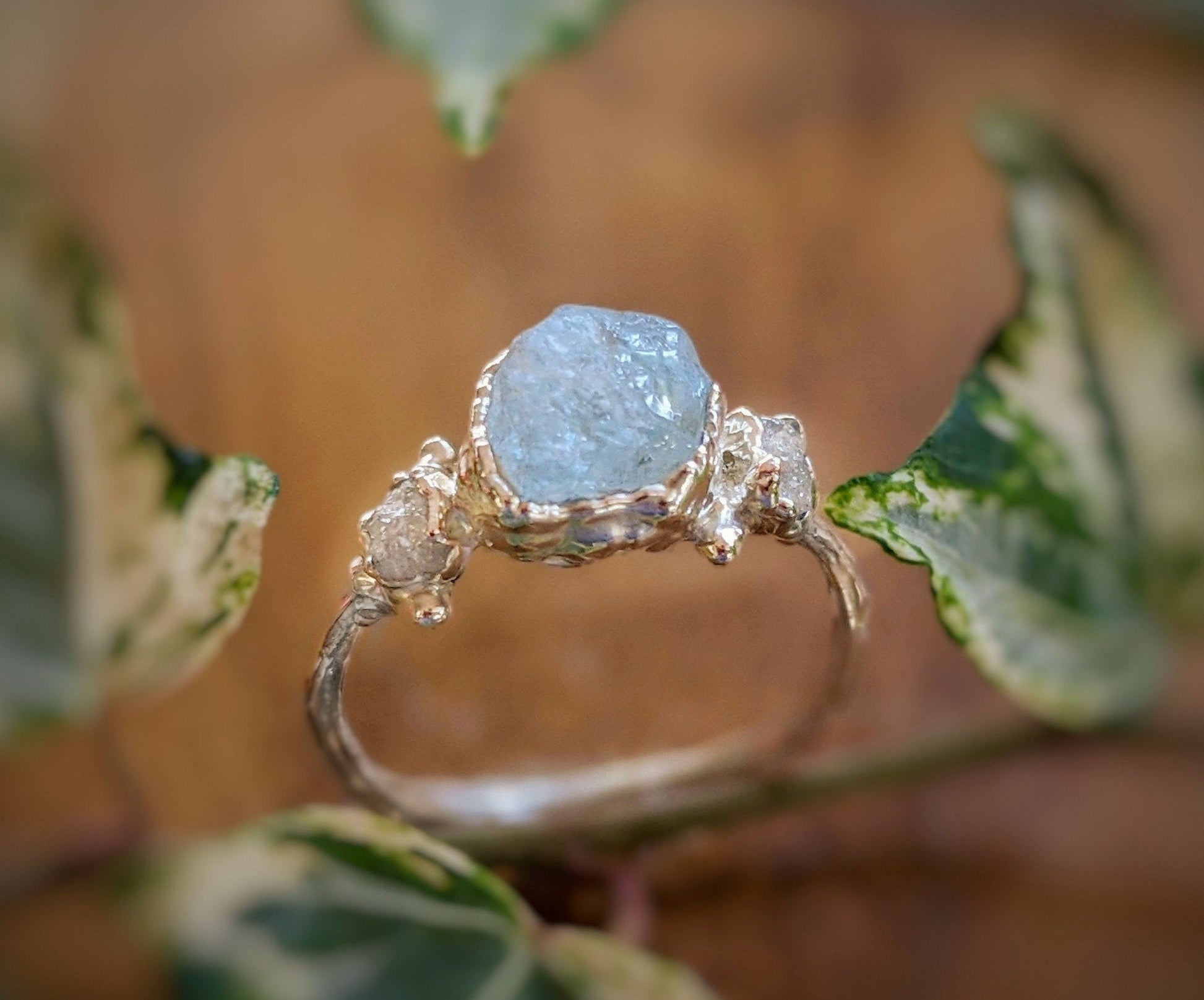 Raw Aquamarine and diamond twig ring set on a unique sterling silver band surrounded by greenery.