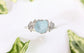 Raw aquamarine and diamond twig ring on a white surface, surrounded by green leaves, featuring a unique design.