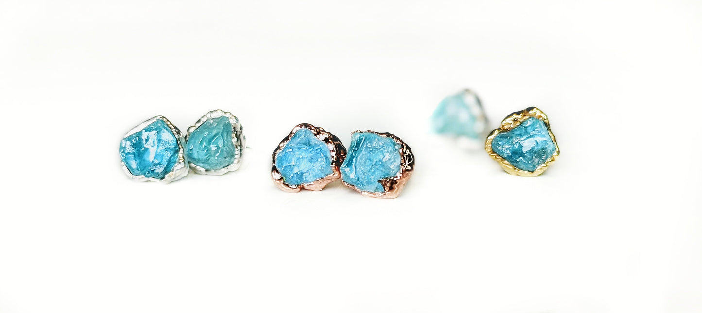Raw Aquamarine stud earrings in gold and silver settings, showcasing unique rough stone shapes and vibrant blue hues.