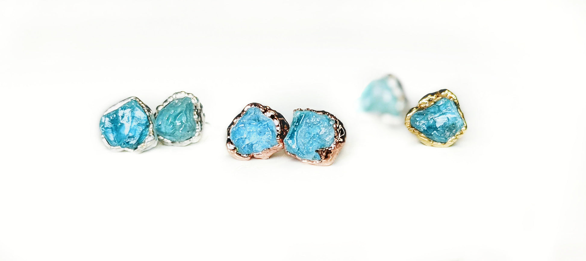Raw Aquamarine stud earrings in gold and silver settings, showcasing unique rough stone shapes and vibrant blue hues.