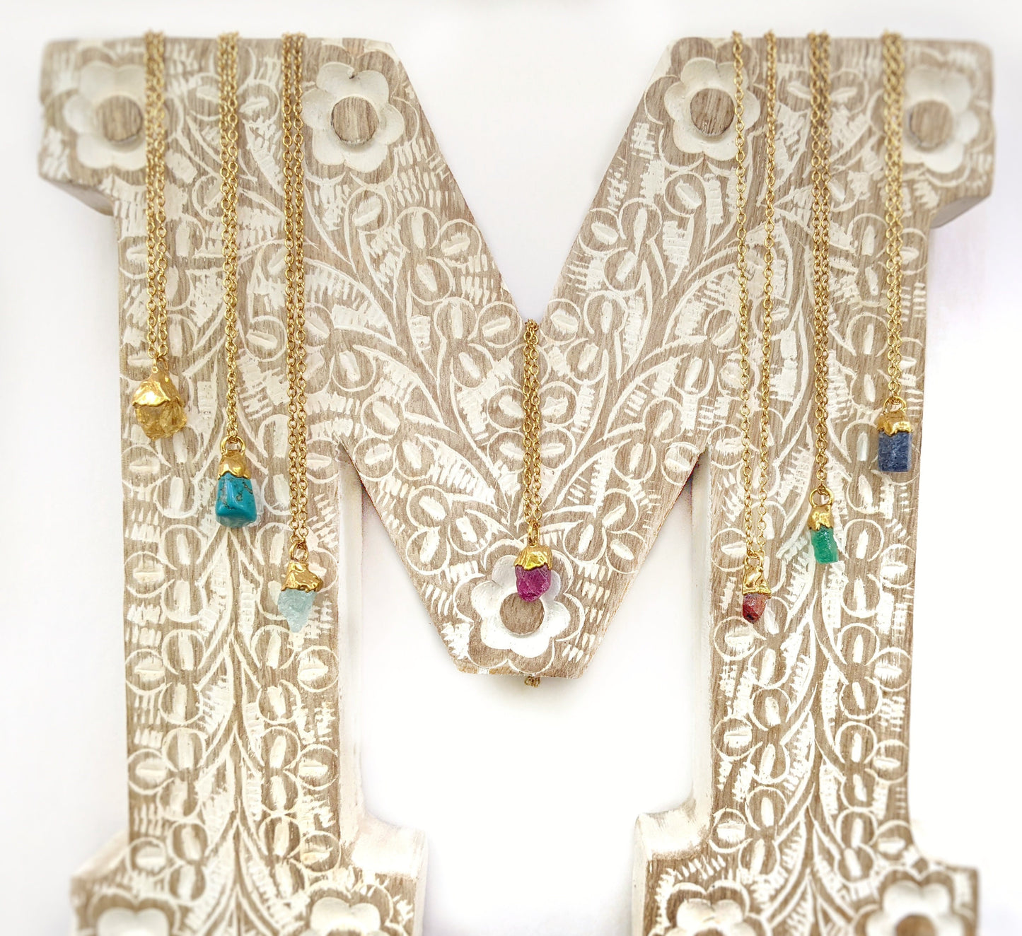Handcrafted raw crystal and gemstone necklaces on a decorative letter M, showcasing vibrant birthstones.