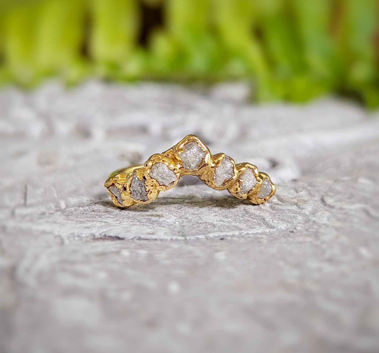 Raw diamond Chevron wedding band on a textured surface with a gold finish, showcasing seven conflict-free diamonds.