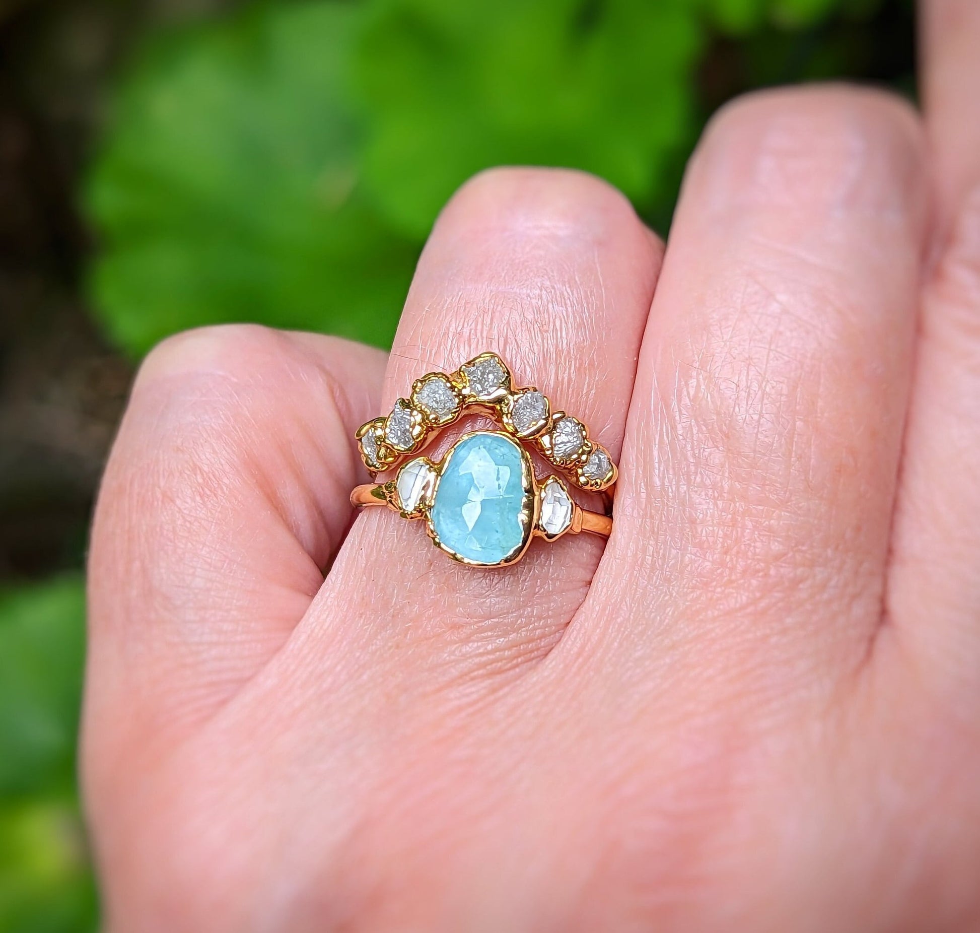 Unique gold Chevron wedding band featuring raw diamonds and an aquamarine stone on a hand outside.