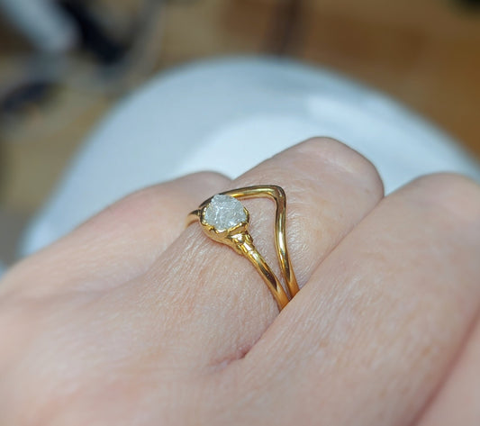 Raw diamond engagement ring set on a hand, featuring a unique uncut diamond and 18k gold chevron band.