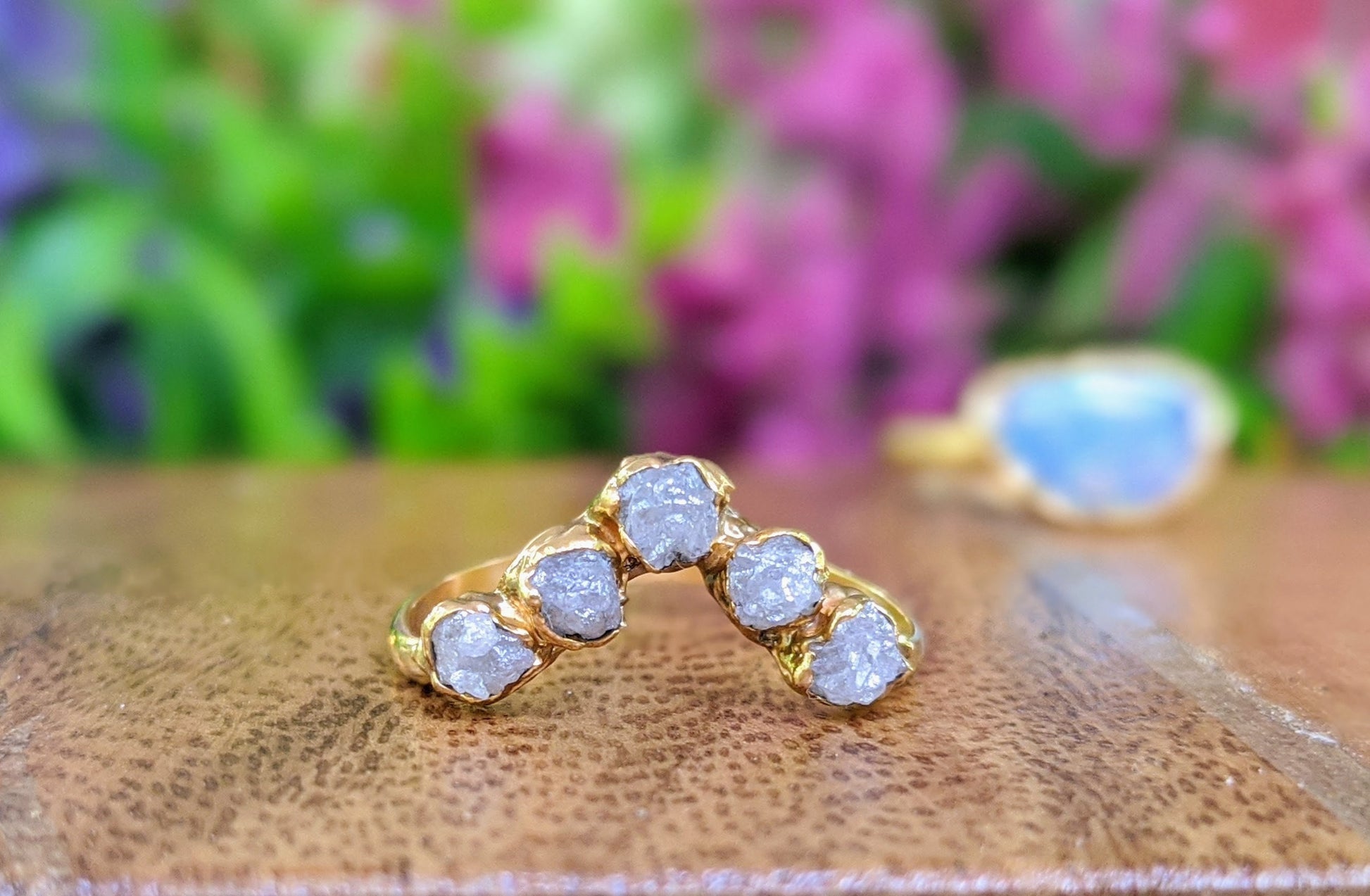 Raw diamond Chevron engagement ring in 18k gold with five conflict-free raw diamonds on a wooden surface.