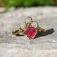 Raw diamond and pink spinel chevron engagement ring on a rocky surface, showcasing unique handcrafted beauty.