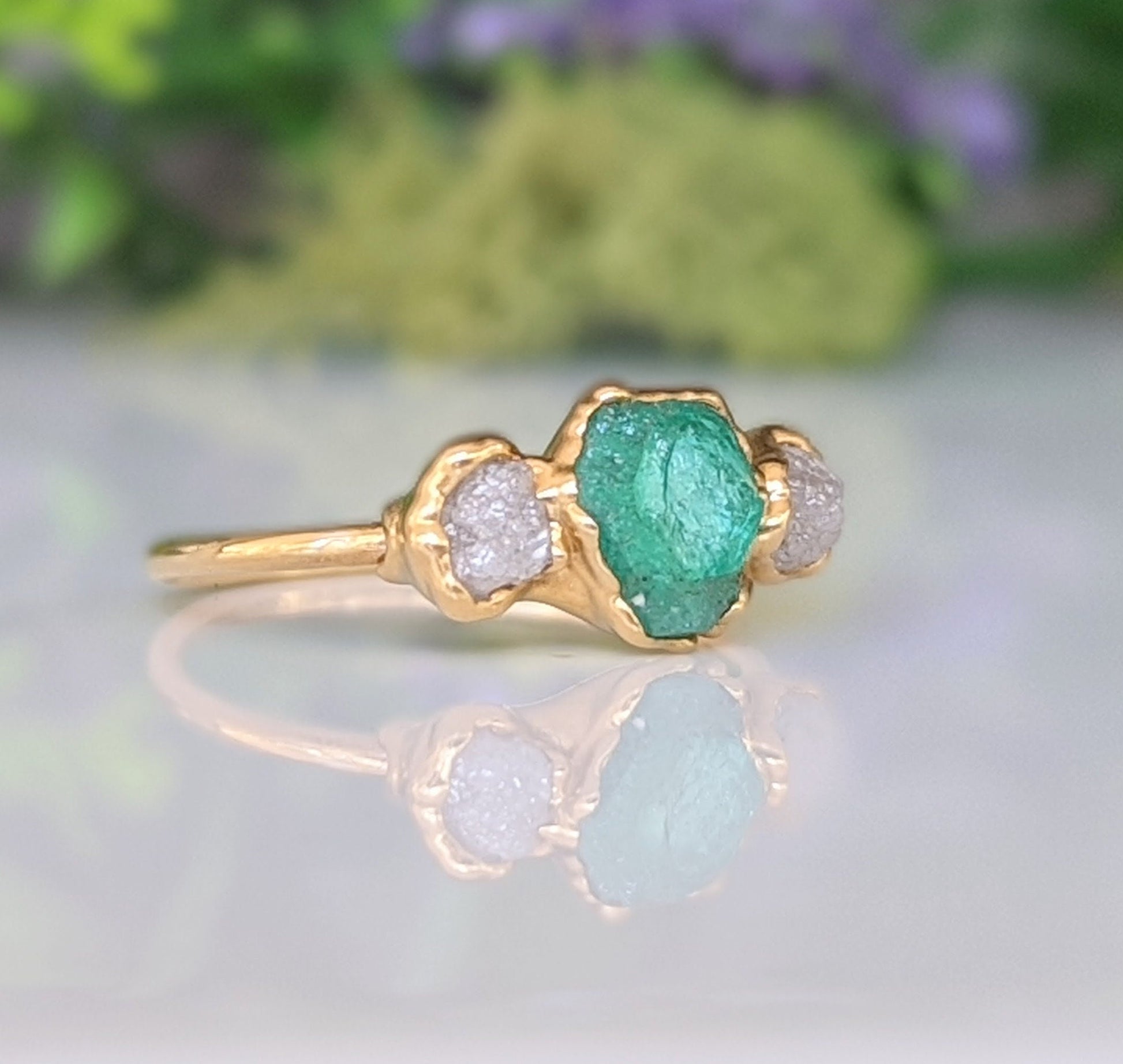 Raw emerald and diamond engagement ring with gold band, symbolizing love and commitment.
