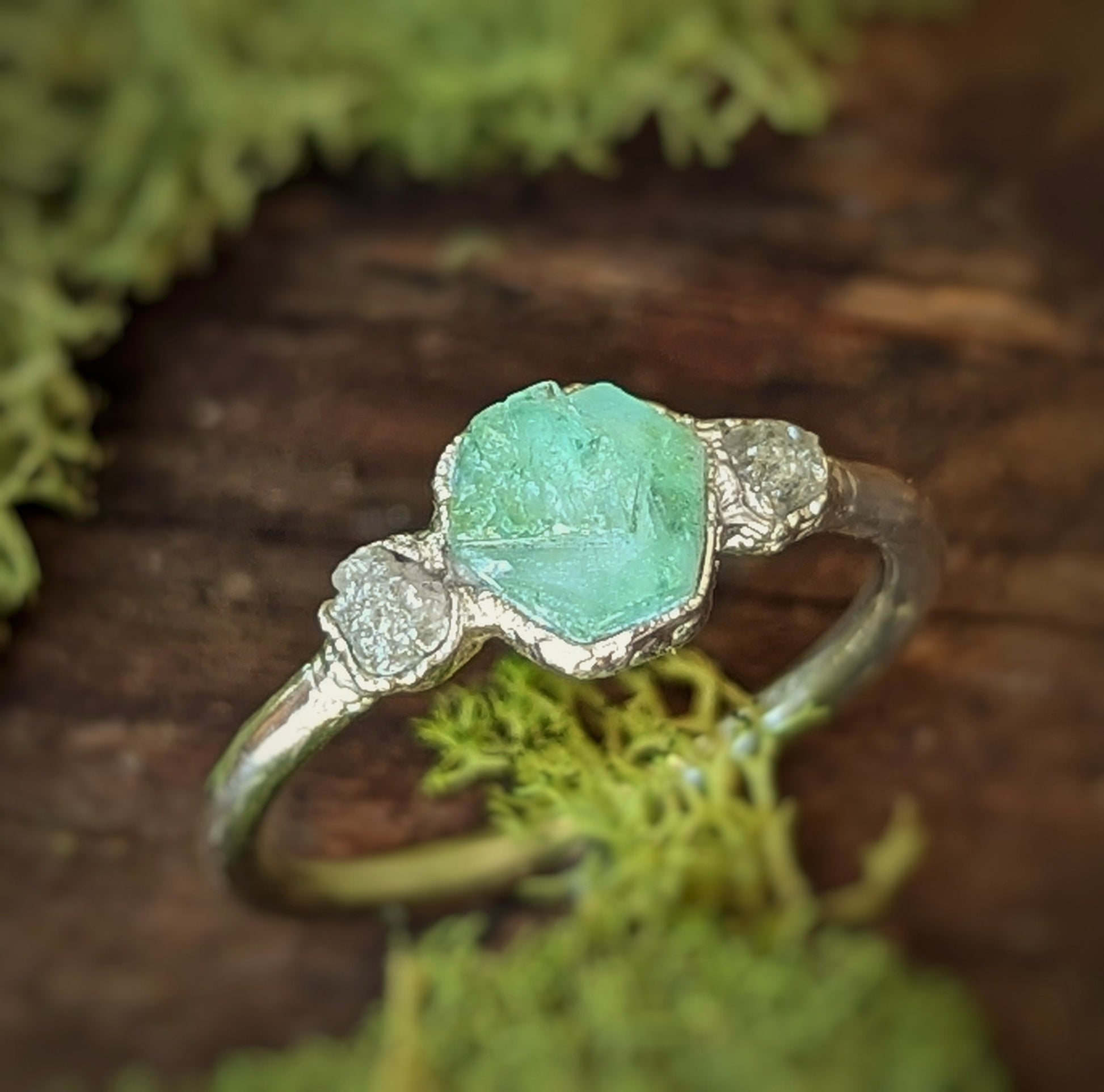 Handcrafted Raw Emerald and Diamond Engagement Ring on mossy background.