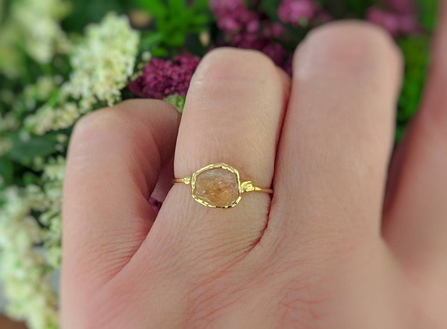 Raw Hessonite Garnet ring on hand, 14k Gold filled band, surrounded by colorful flowers.