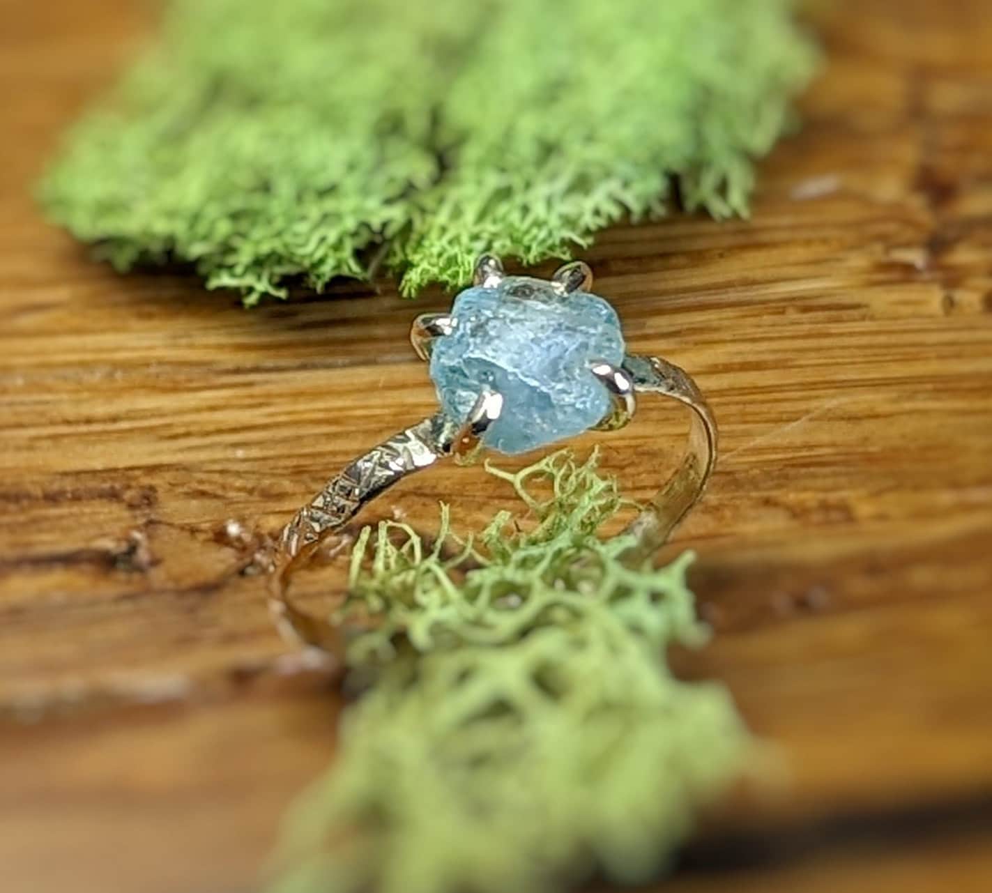 Raw Montana Sapphire ring with textured gold band against natural moss background.