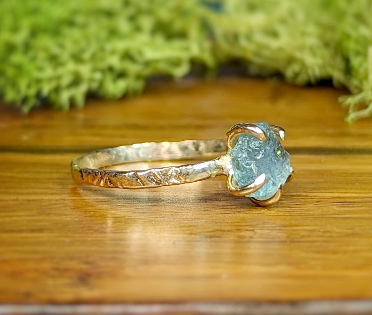 Raw Montana Sapphire engagement ring with textured gold band, showcasing teal-blue stone for a rustic, unique look.