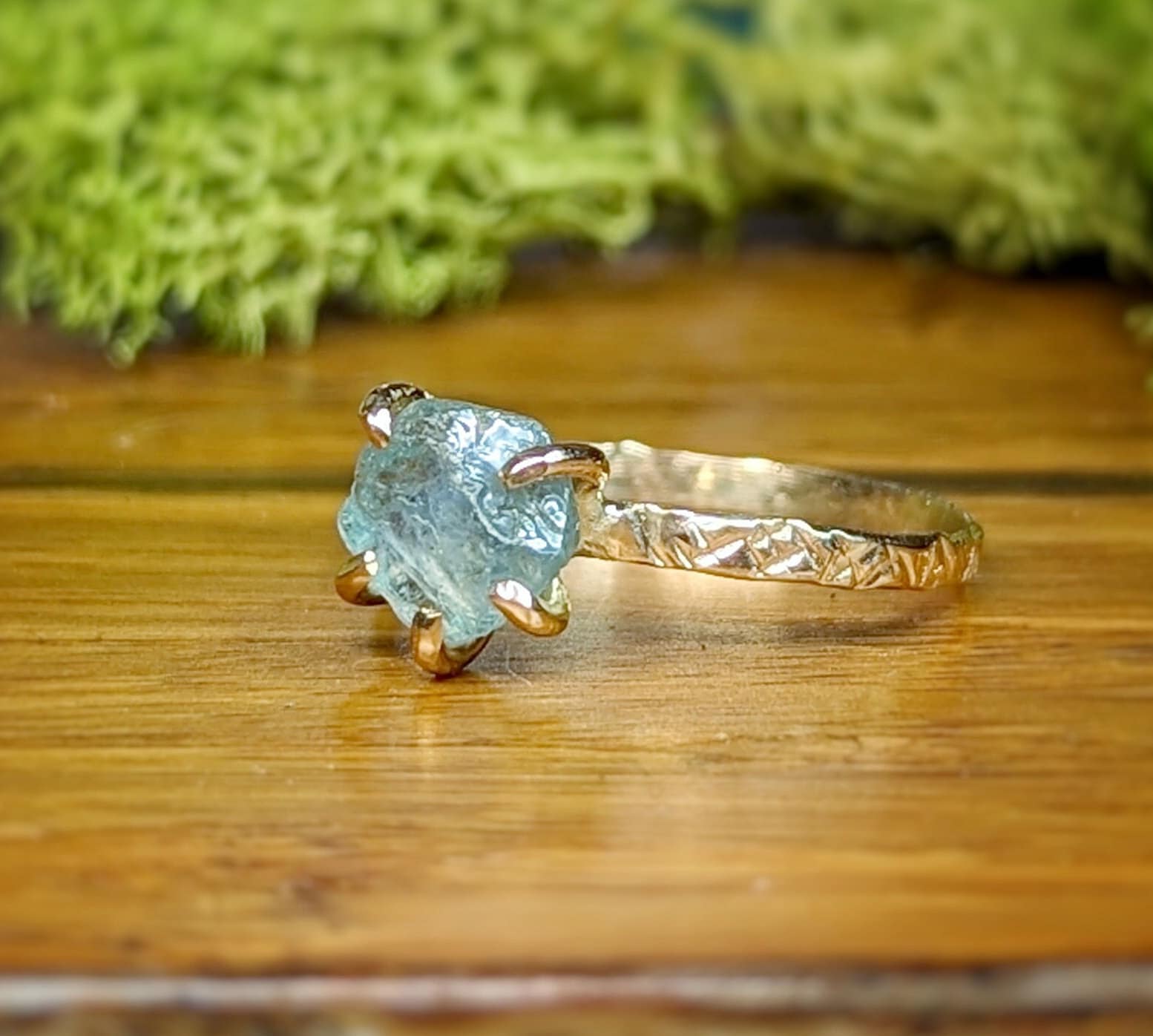 Teal-blue raw Montana Sapphire engagement ring with textured gold band, showcasing a unique rustic elegance.