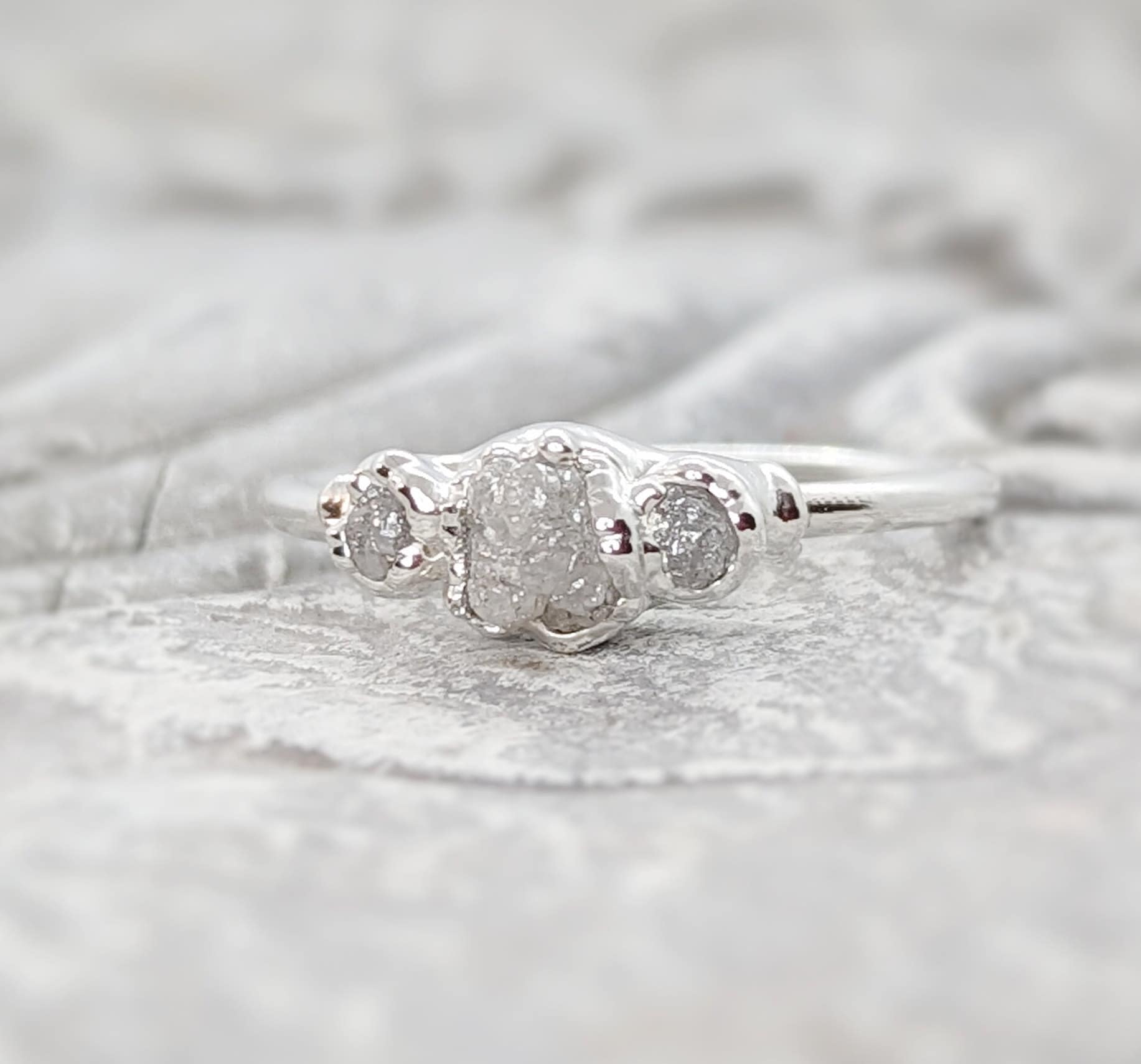 Handcrafted raw diamond engagement ring with one large and two smaller raw diamonds, set in silver.