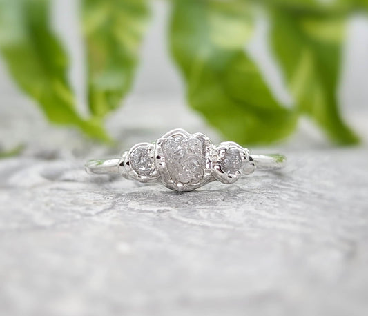 Handcrafted raw diamond engagement ring featuring one large and two smaller raw diamonds on a silver band.