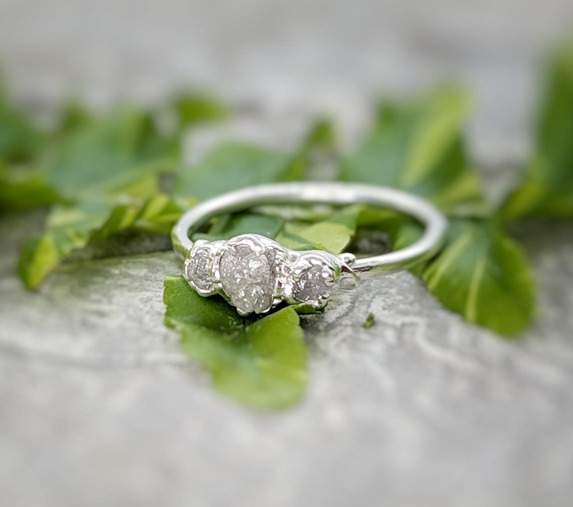 Raw natural diamond engagement ring with unique handcrafted design nestled in green leaves.
