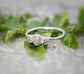Raw natural diamond engagement ring with unique handcrafted design nestled in green leaves.
