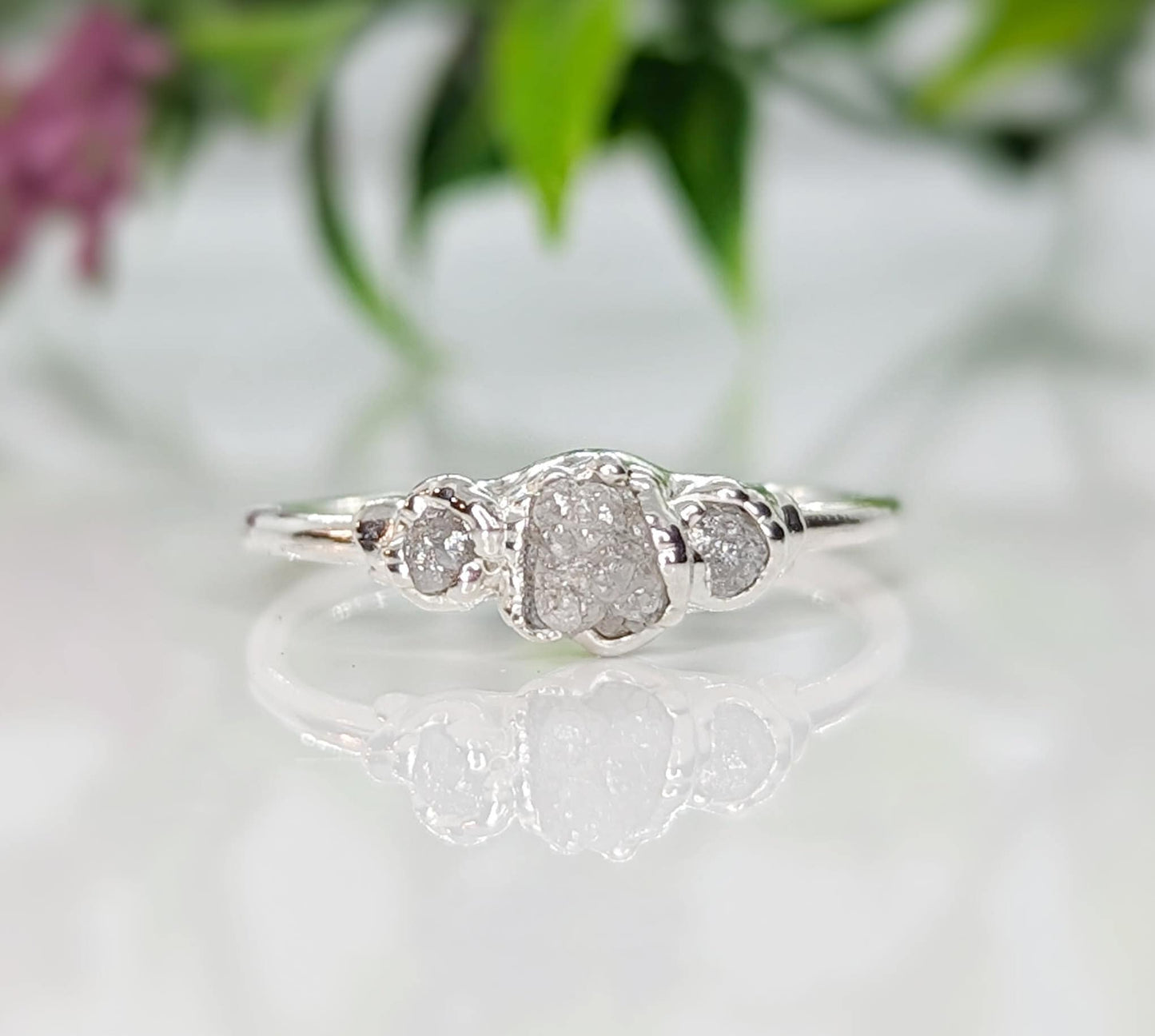 Handcrafted raw diamond engagement ring featuring a large center diamond with two smaller diamonds on a silver band.