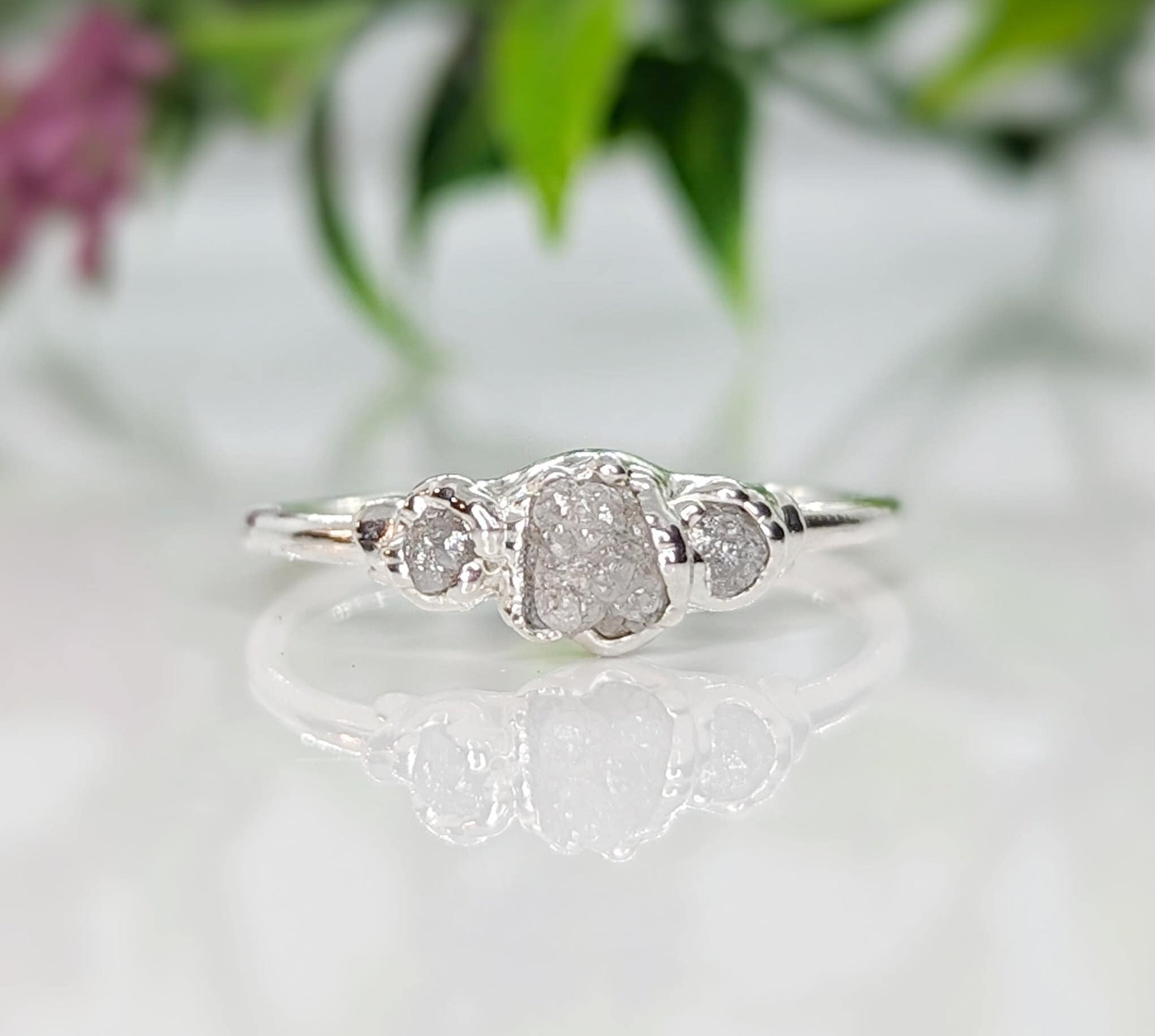 Handcrafted raw diamond engagement ring featuring a large center diamond with two smaller diamonds on a silver band.