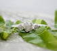 Raw natural diamond engagement ring with a large diamond and two smaller diamonds, surrounded by green leaves.