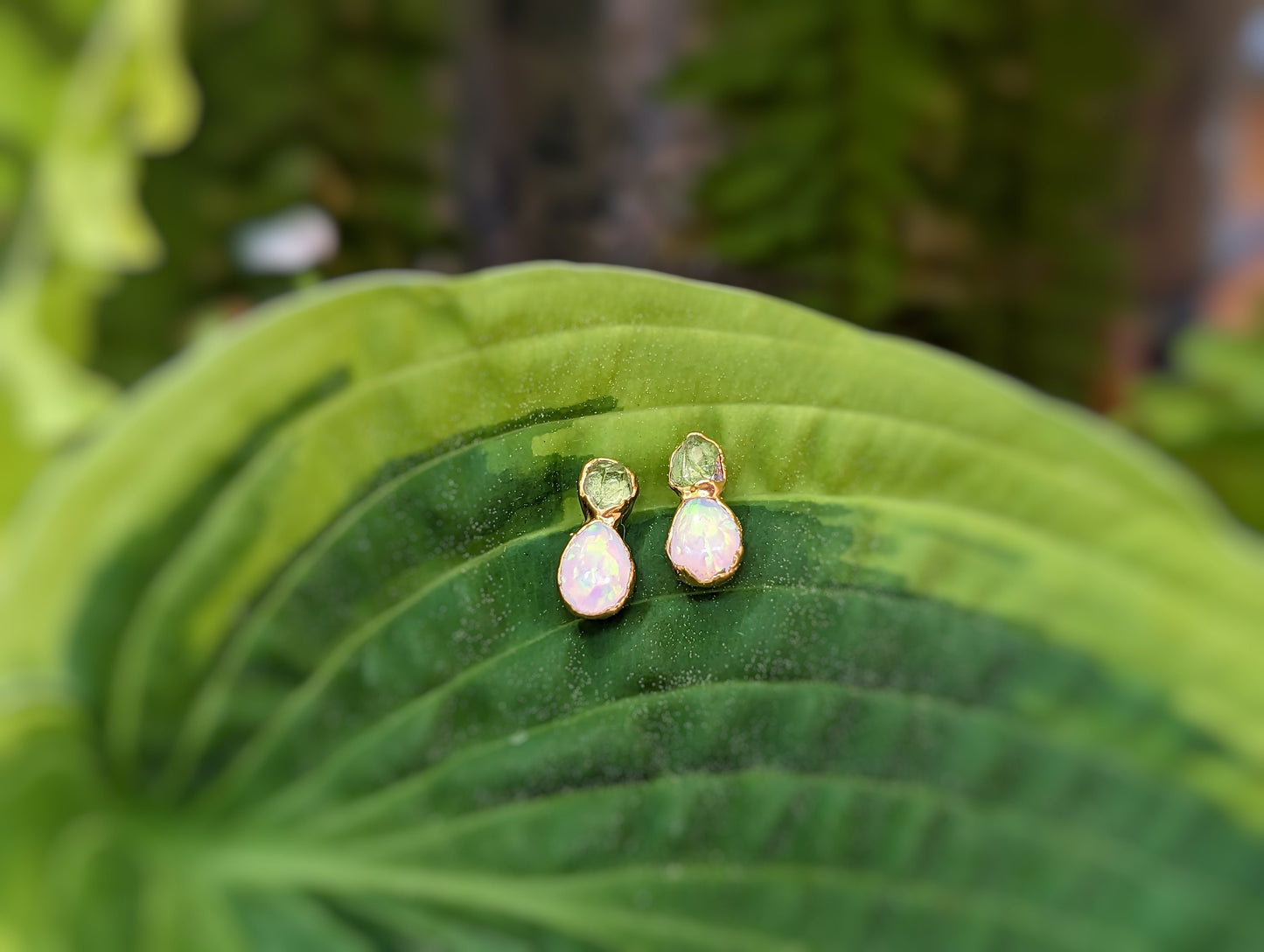 Raw Peridot and Opal stud earrings resting on a green leaf, showcasing their elegant and rustic design.