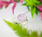 Handcrafted raw pink Morganite ring set on a silver band, surrounded by greenery and floral accents.