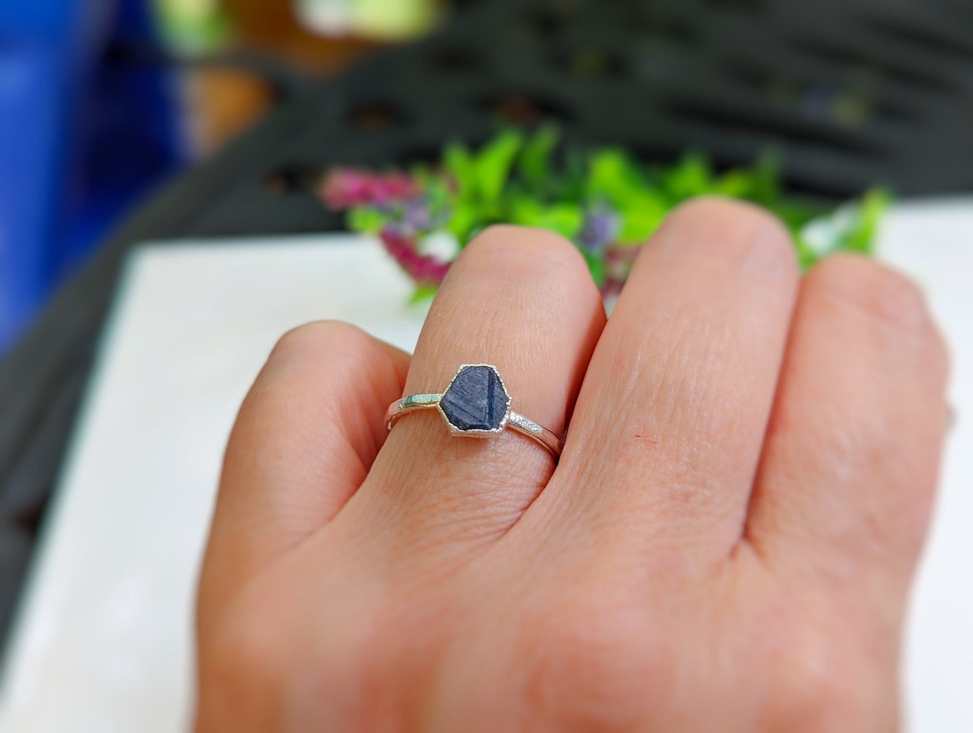 Handcrafted raw sapphire ring on a finger, featuring a unique hexagonal design on a sterling silver band.